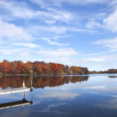 Calm Minnesota lake with a dock and trees in full autumn color under blue sky and clouds